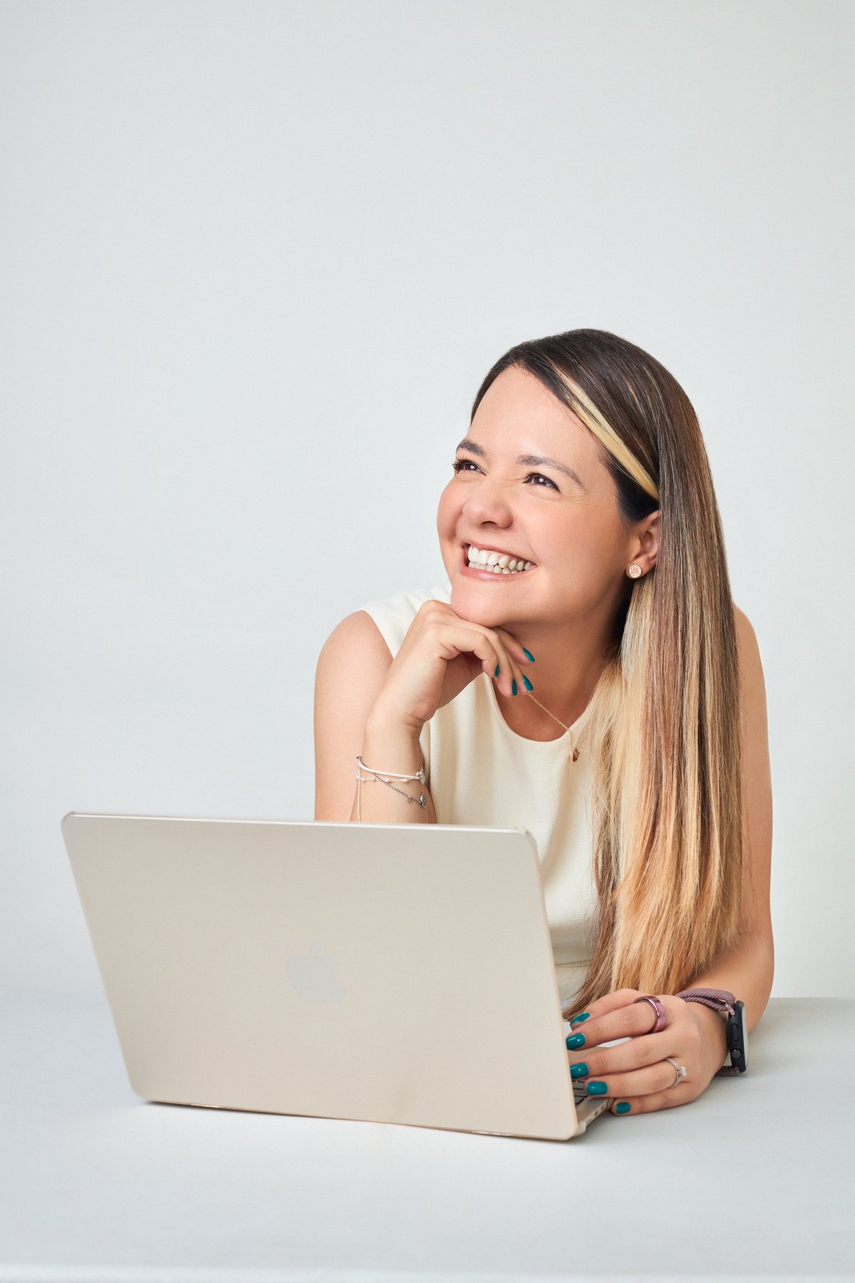 Young woman with long brown hair smiling while working on a laptop against a white background